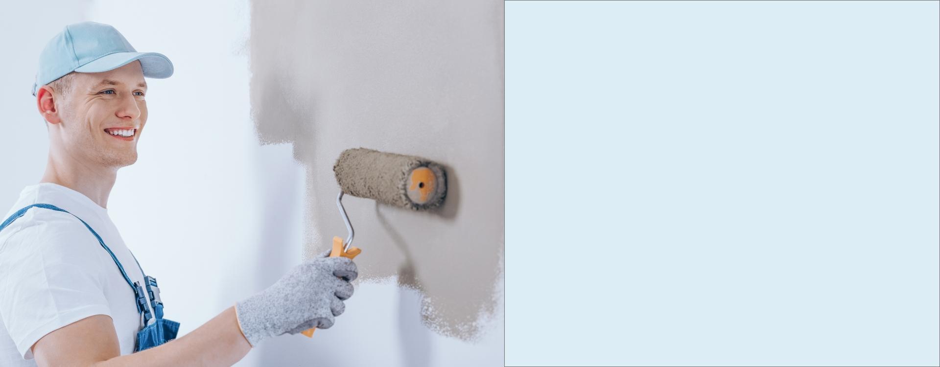 Uśmiechnięty pracownik maluje ścianę przy pomocy wałka Slide B - 2