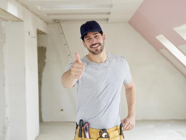 Uśmiechnięta osoba z uniesionym kciukiem do góry w pomieszczeniu podczas remontu